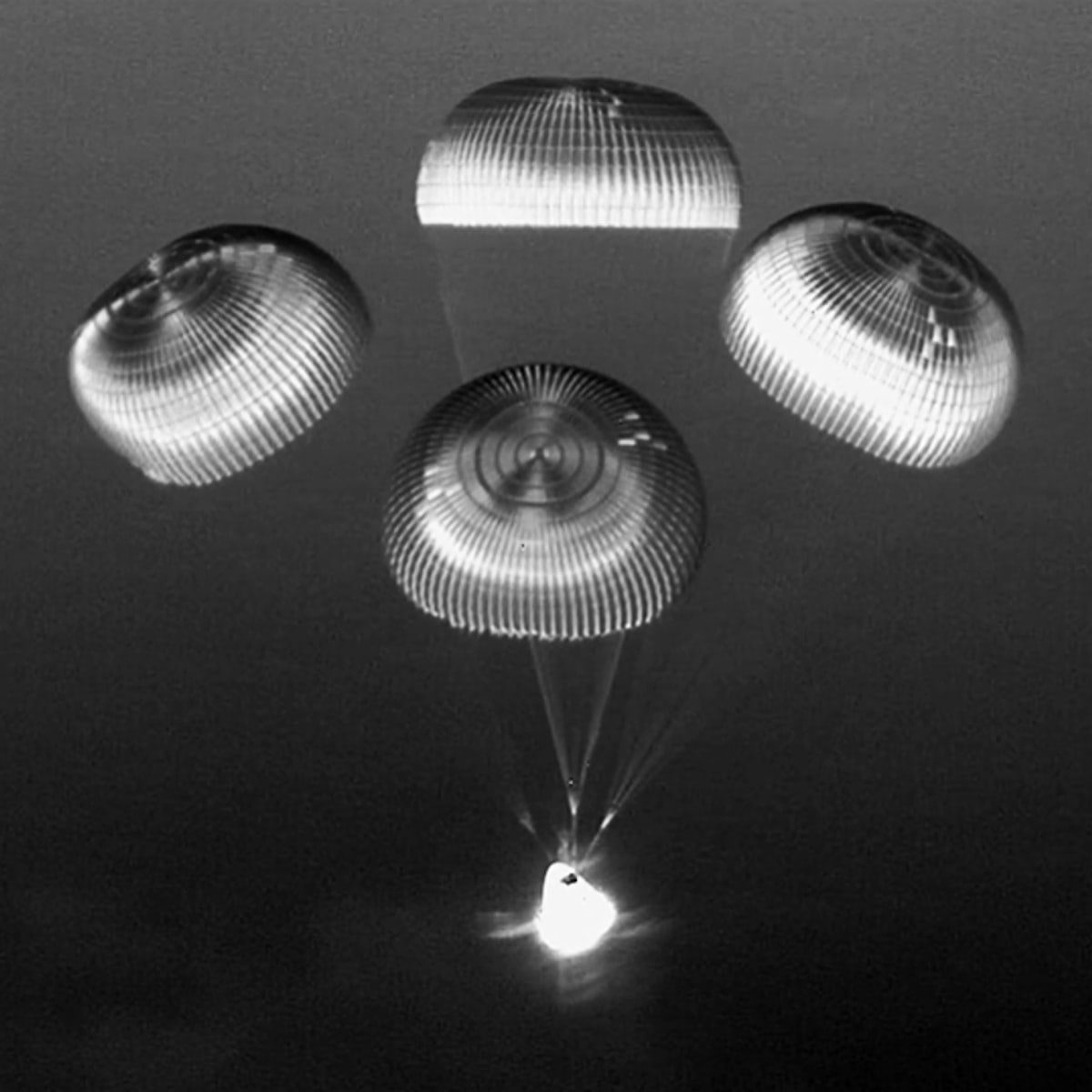 Grayscale sensor image of a crew capsule descending under four main parachutes