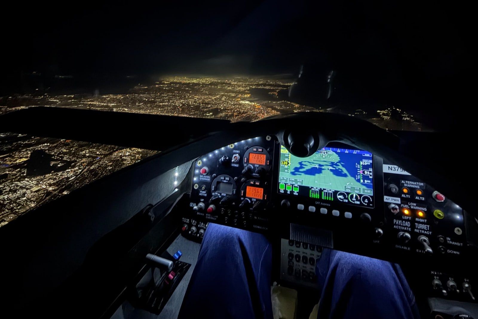 Lit Mobius instrument panel at altitude at night, city lights along the San Diego coastline below